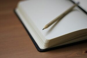 Pencil resting across the blank pages of an open notebook