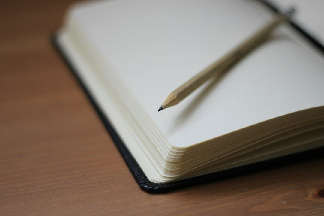 Pencil resting across the blank pages of an open notebook