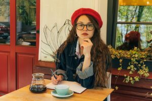 Writer in a red beret taking notes at a café table